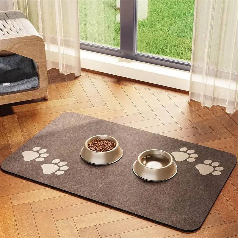 Brown suede-look absorbent pet feeding mat with a paw print at each end and two gold bowls, by a patio door.
