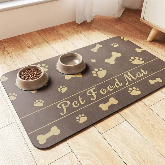 Brown absorbent pet feeding mat printed Pet Food Mat with gold bones and paws, holding a food bowl and a water bowl on a wood floor.