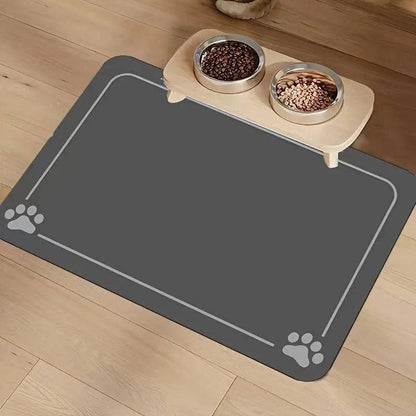 Dark gray absorbent pet feeding mat with a thin border line and paw prints in two corners under a raised double bowl.