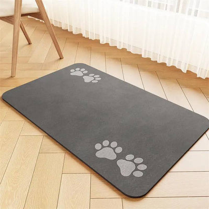 Dark gray suede-look absorbent pet feeding mat with a light paw print at each end, on a herringbone floor.
