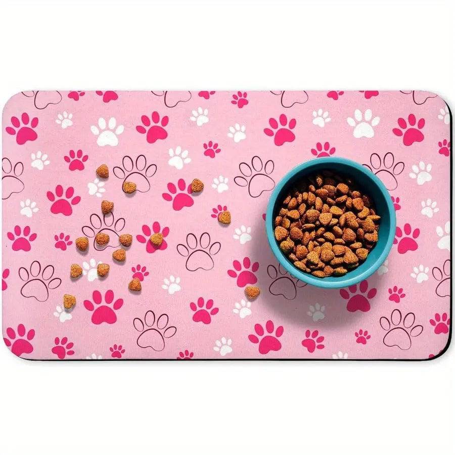 Pink absorbent pet feeding mat with pink and white paw prints, a teal food bowl and scattered kibble.