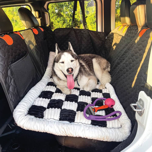 A husky lying on the checkered Noblias back seat dog bed mat spread across a car's rear bench.