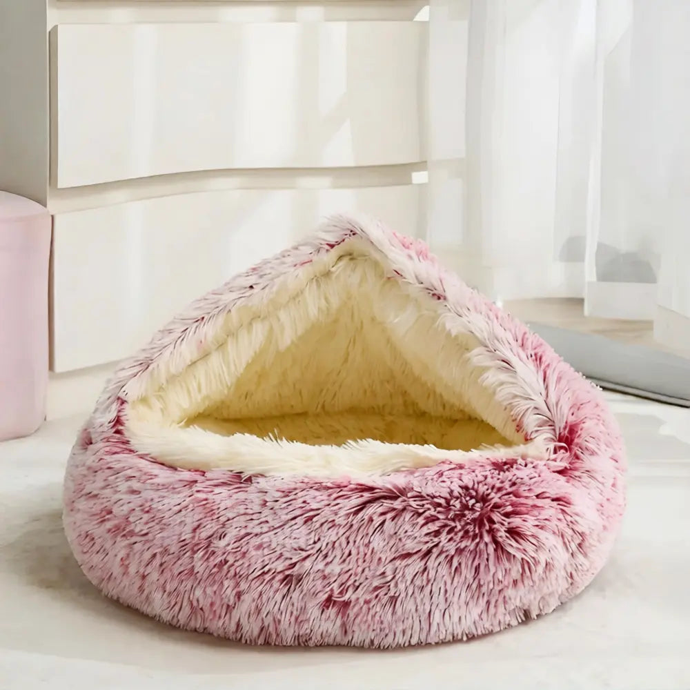 Pink Noblias calming hooded cave pet bed shown beside a bedroom window.