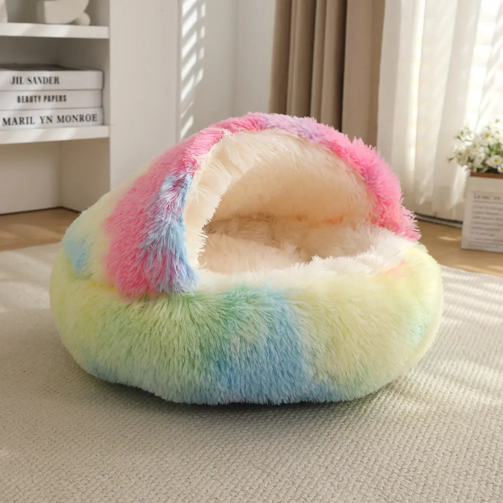 Rainbow Noblias calming hooded cave pet bed in pink, blue and yellow plush on a bedroom floor.
