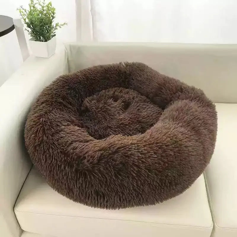 Dark brown long plush round calming dog bed on a white sofa