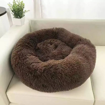 Dark brown long plush round calming dog bed on a white sofa