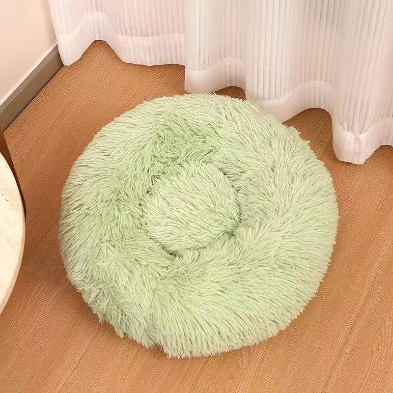 Light green long plush round calming dog bed on a wooden floor