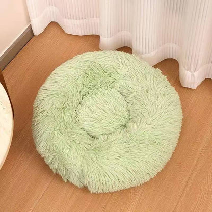 Light green long plush round calming dog bed on a wooden floor