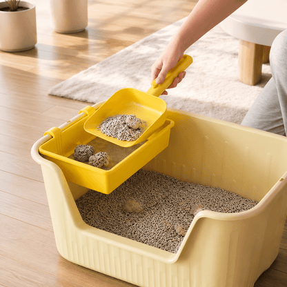 A hand lifting the yellow cat litter sifting tray out of a cream litter box with clumps caught in the mesh.
