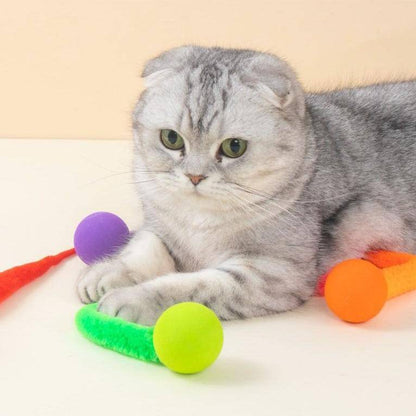 Scottish Fold cat lying beside the colorful Noblias cat toy balls with fuzzy worm tails