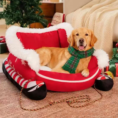A golden retriever in a green scarf lying in the red Christmas sleigh pet bed beside a Christmas tree.