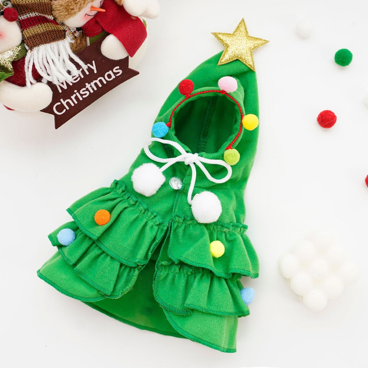 Green Christmas tree pet costume laid flat, showing the tiered ruffles, pom poms and star-topped hood.