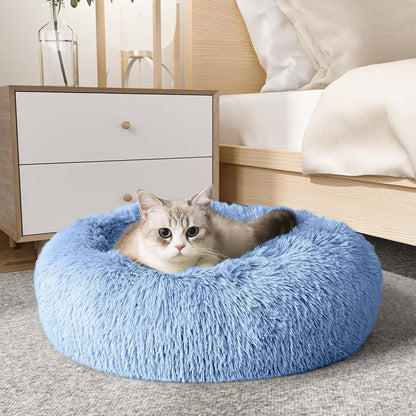 Light blue Noblias cloud calming donut bed with a cat settled inside beside a bed.