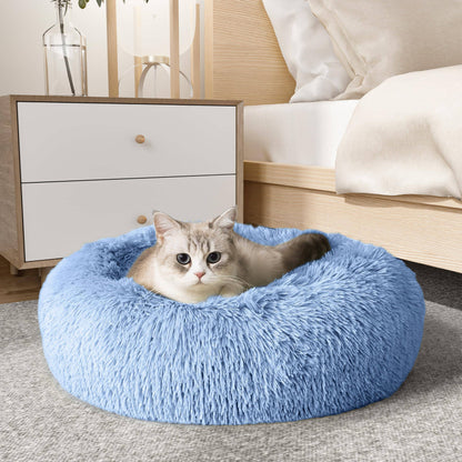 Cat resting in the light blue Noblias cloud calming donut bed beside a bedroom nightstand.