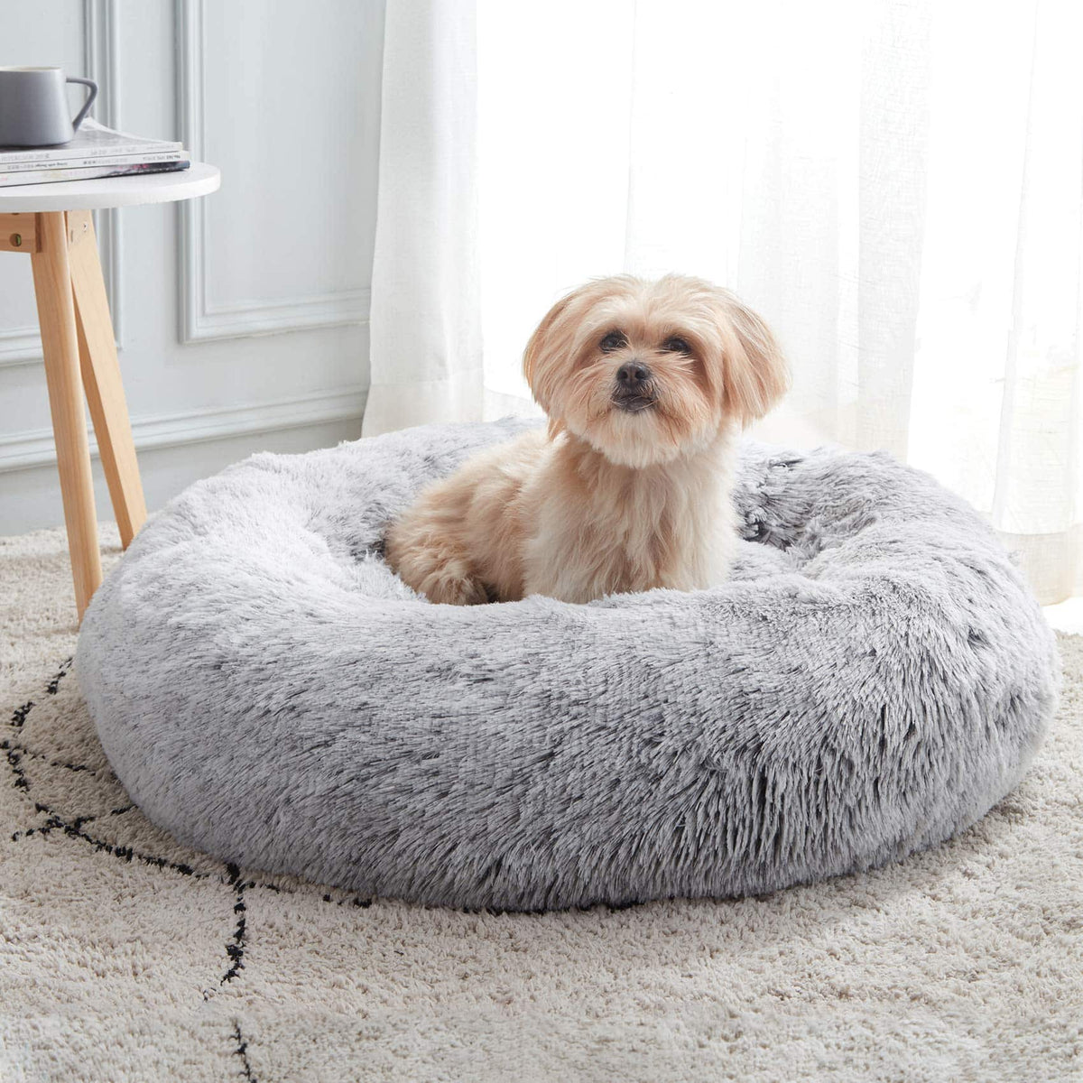 Light gray Noblias cloud calming donut pet bed with a small shih tzu sitting inside on a rug.