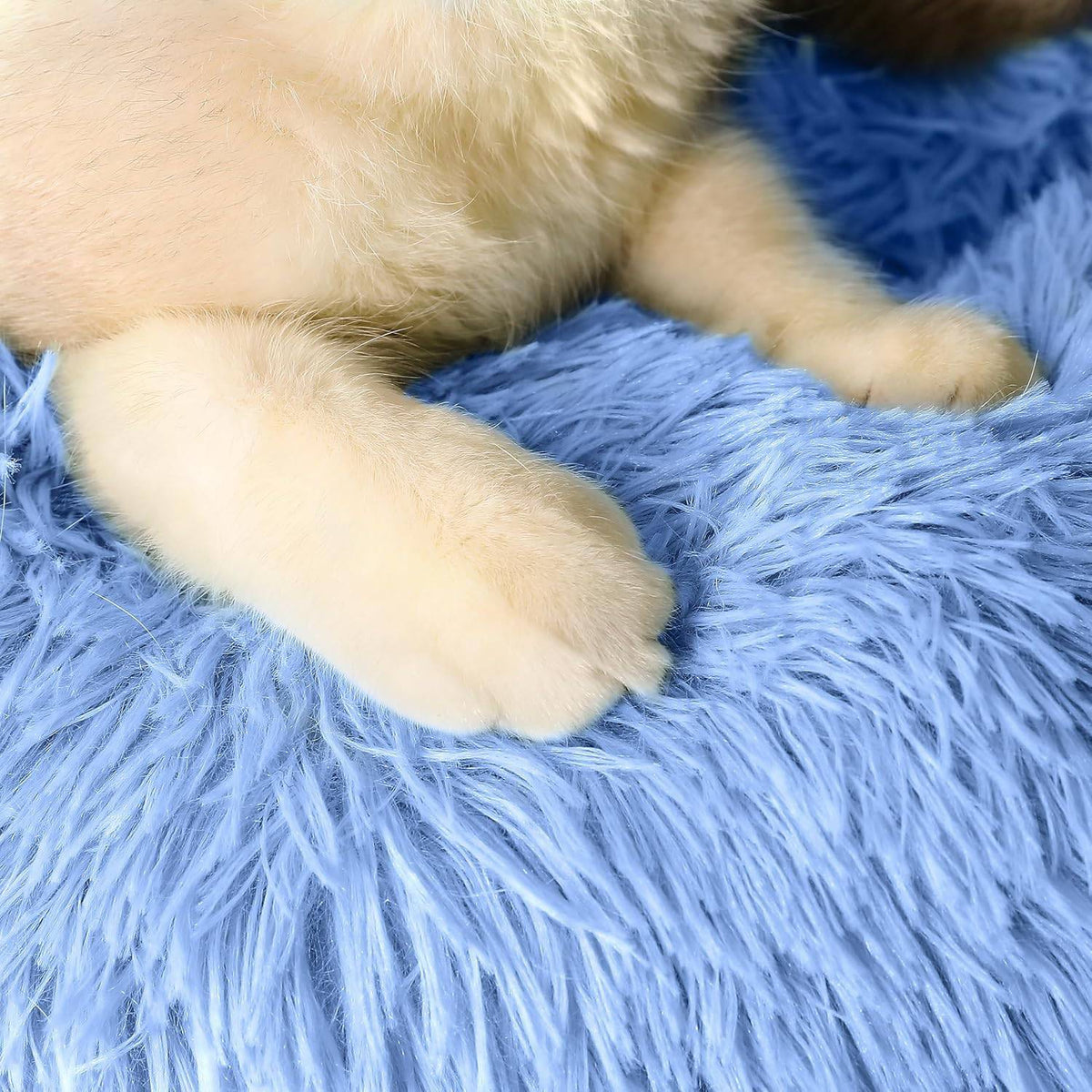Close up of a cat's paw sinking into the long plush faux fur of the Noblias cloud calming donut bed.