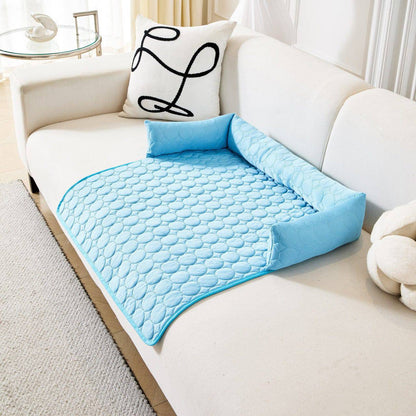 Blue Noblias cooling dog couch cover laid across a white sofa, with the quilted mat draping over the front edge of the seat and the bolster forming a raised back and side.