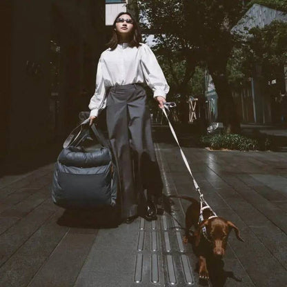 The gray Noblias dog car seat bed carried over the shoulder like a bag while walking a dachshund.