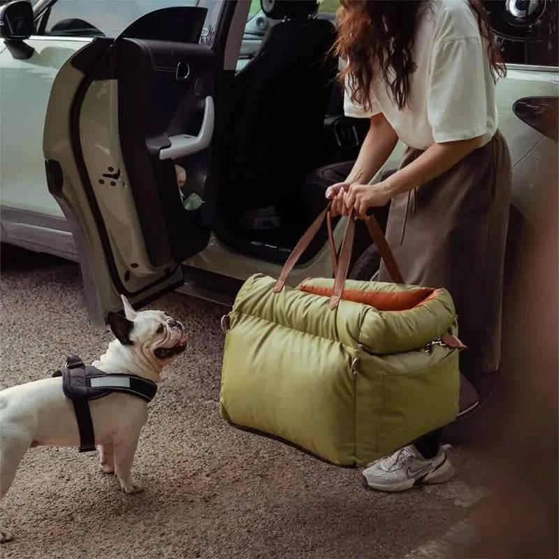 An owner lifting the green Noblias dog car seat bed by its handles beside an open car door.