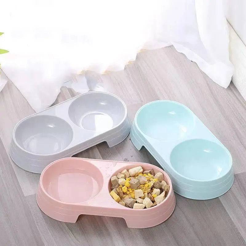 Three double pet bowl sets in gray, pink and blue arranged on a wooden floor with food in one