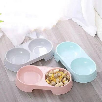 Three double pet bowl sets in gray, pink and blue arranged on a wooden floor with food in one