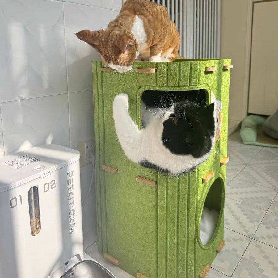 One cat sitting on top of the Noblias felt cat house while another climbs into the upper cave.