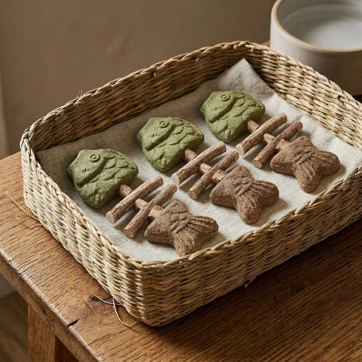 Several Noblias fish bone cat dental chew toys laid out in a woven basket.
