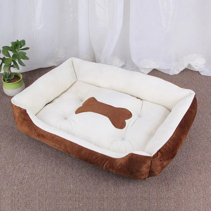 Brown fleece bolster dog bed with a cream cushion and a brown bone applique, beside a potted plant.