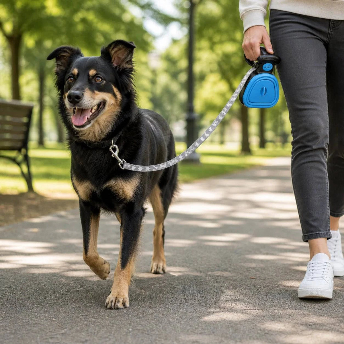 Woman walking a black dog with the blue foldable pooper scooper clipped to the leash handle.