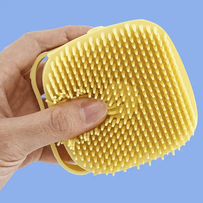 Yellow Noblias handheld silicone dog bath brush held in a hand, showing the soft bristle face.