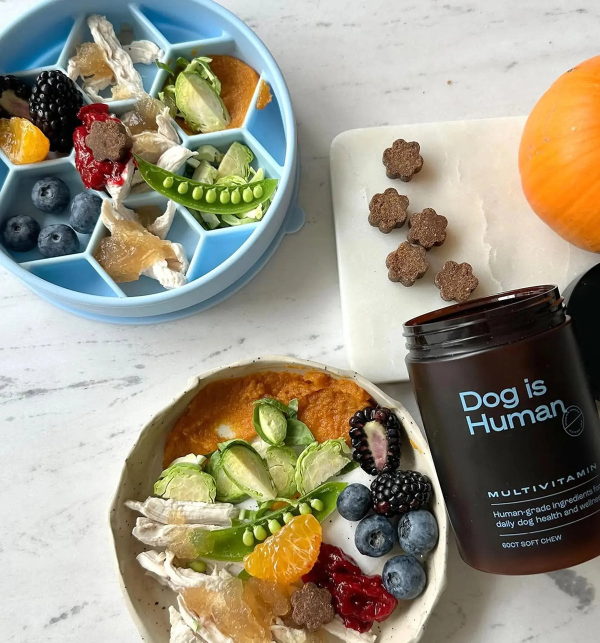 Blue Noblias honeycomb slow feeder dog bowl holding fresh food in separate cells, including berries, orange, peas and cooked meat.