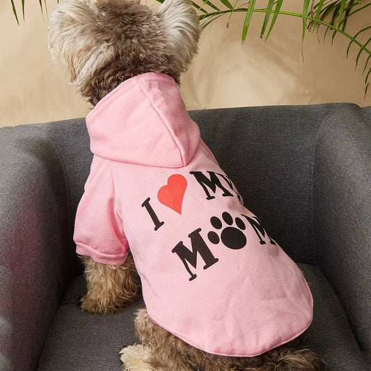 Poodle mix wearing the pink I love my mom dog hoodie on a gray armchair.