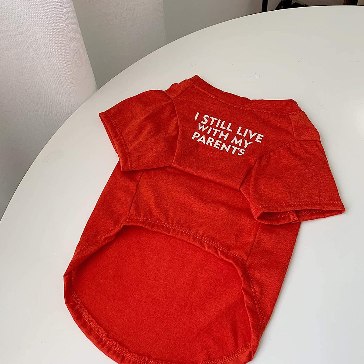 Red I Still Live With My Parents dog shirt laid flat on a table, showing the round neck, short sleeves and curved hem