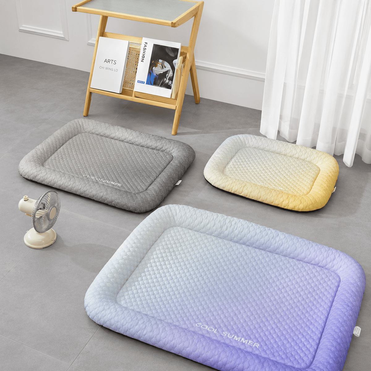 The gradient black, gradient yellow and gradient blue ice silk cooling mats laid out together beside a desk fan.