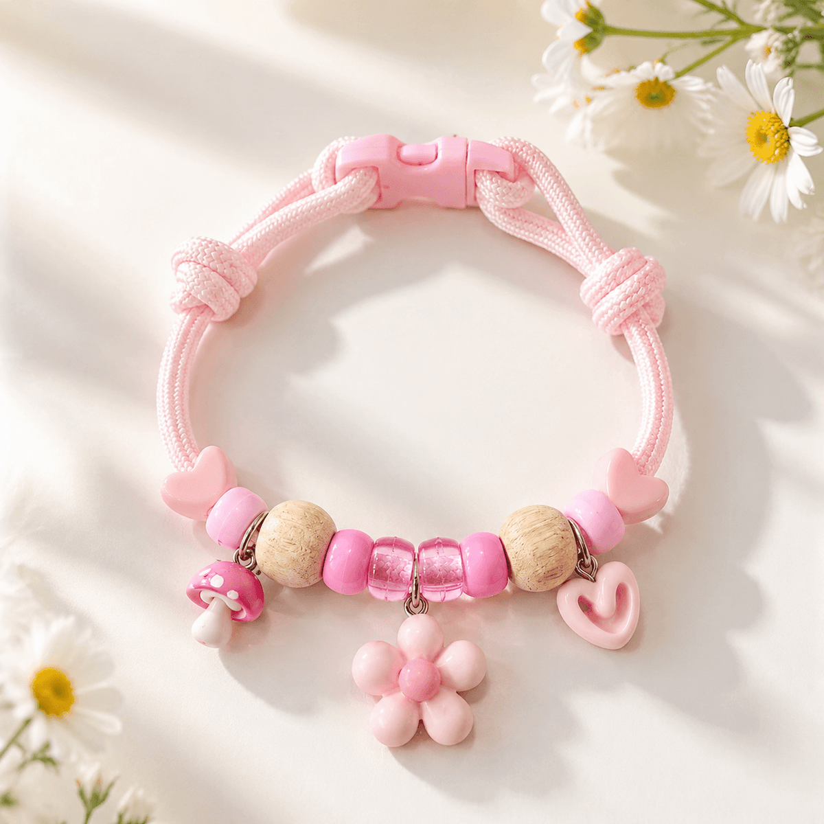 Pink insect repellent pet collar with natural wood beads, a flower charm, a heart charm and a quick release buckle, laid on a pale surface with daisies.