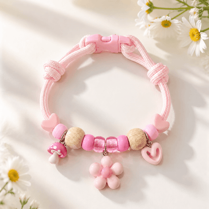 Pink insect repellent pet collar with natural wood beads, a flower charm, a heart charm and a quick release buckle, laid on a pale surface with daisies.