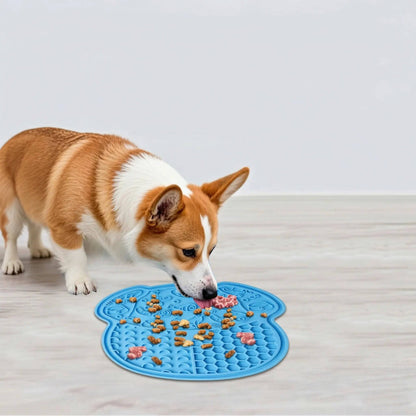 Corgi licking treats off the blue dog-head-shaped lick mat on a wood floor.