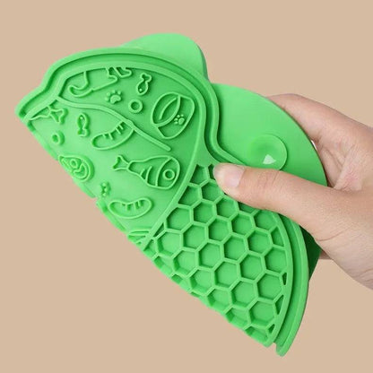 Hand holding the green lick mat to show the embossed food-shape zone above and the honeycomb grid zone below.