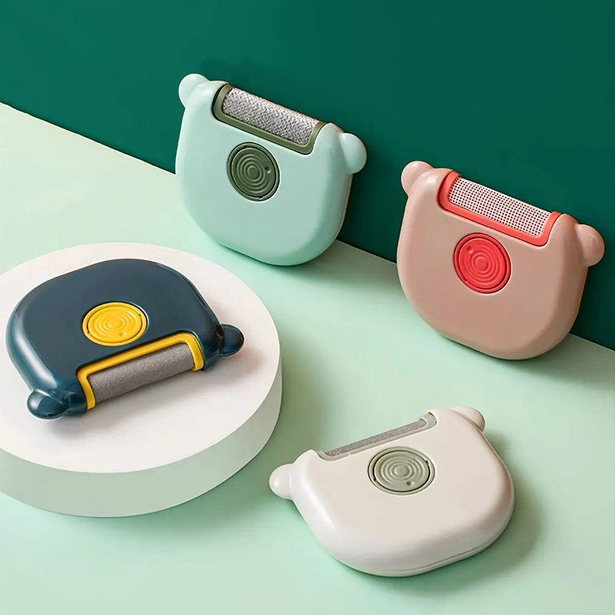 Mini pet hair remover brushes in green, pink, navy with yellow and cream on a two-tone background.