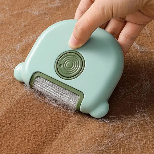 Hand using the green mini pet hair remover brush on a brown blanket covered in pet hair.