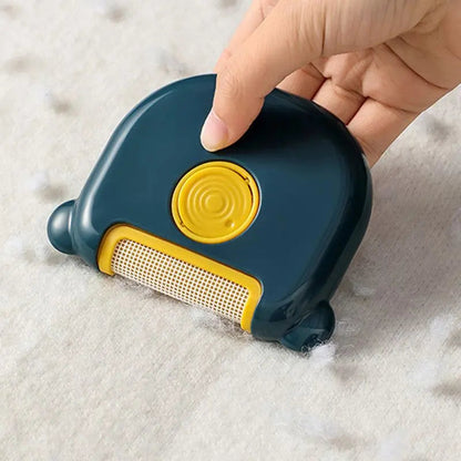 Hand using the navy mini pet hair remover brush on a white fleece blanket.