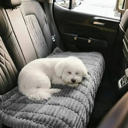 Bichon asleep on the gray ribbed plush cover spread over a car back seat.