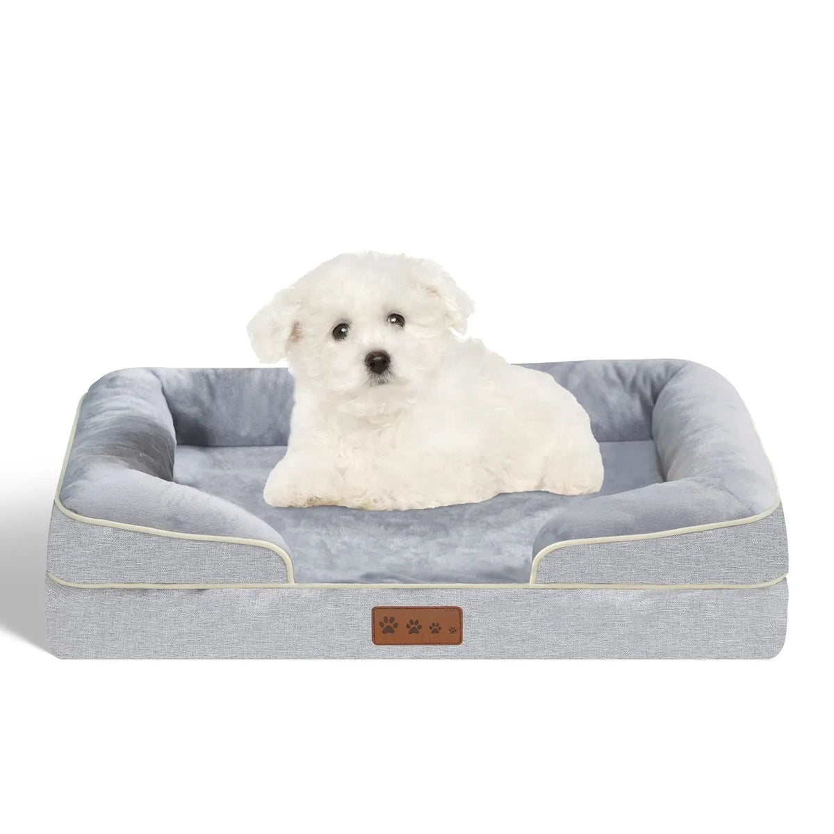 Small white dog sitting on the grey orthopedic dog bed against a white background.