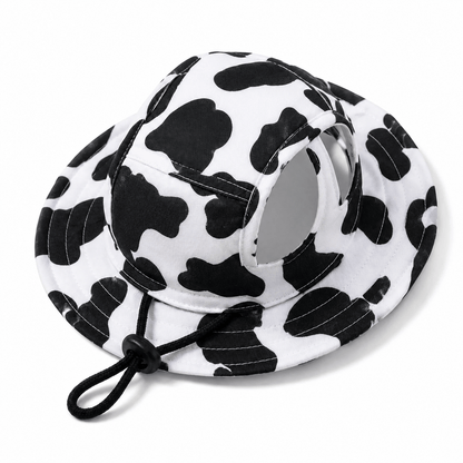The black and white cow print hat photographed alone on a white background with the chin cord hanging loose.