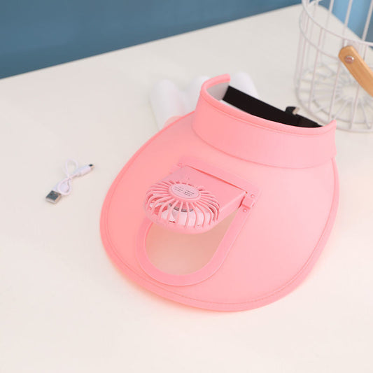 Pink pet sun visor with a small fan clipped to the brim, shown on a white table beside its USB charging cable.