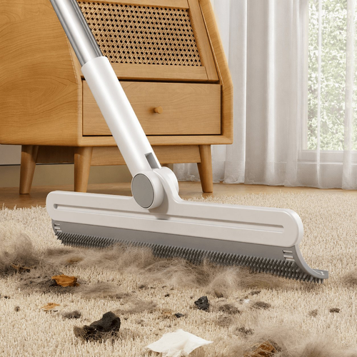 Pet hair removal broom with a white telescopic handle sweeping fur and debris off a beige carpet.