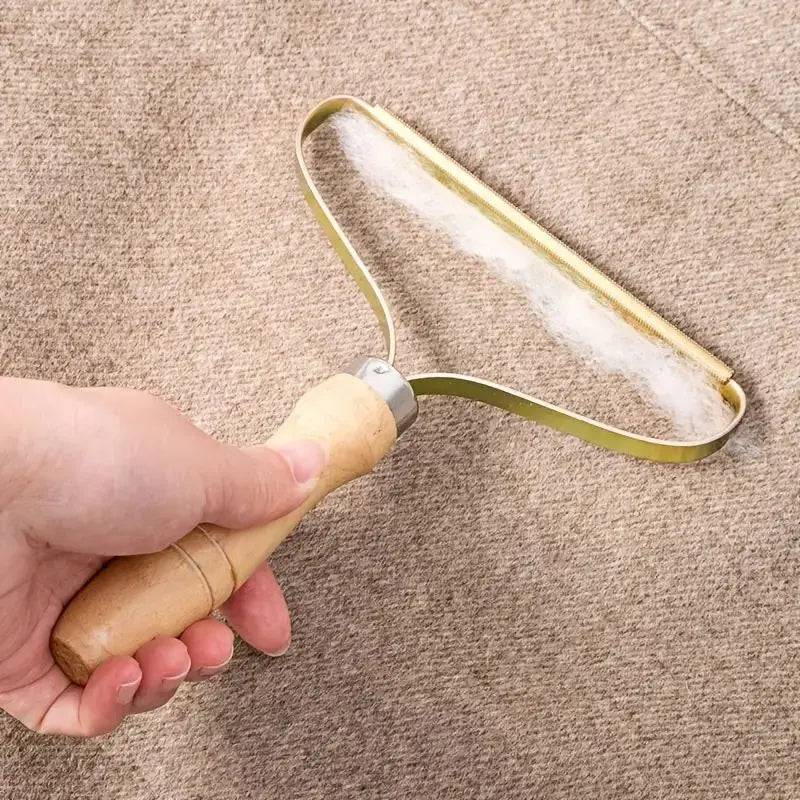 Hand working the fabric shaver across a camel wool coat with fluff gathering along the brass edge.