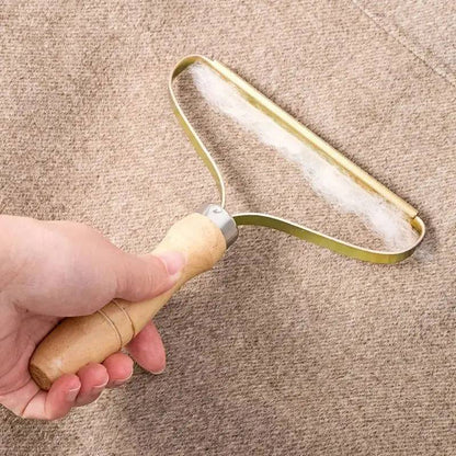 Hand working the fabric shaver across a camel wool coat with fluff gathering along the brass edge.