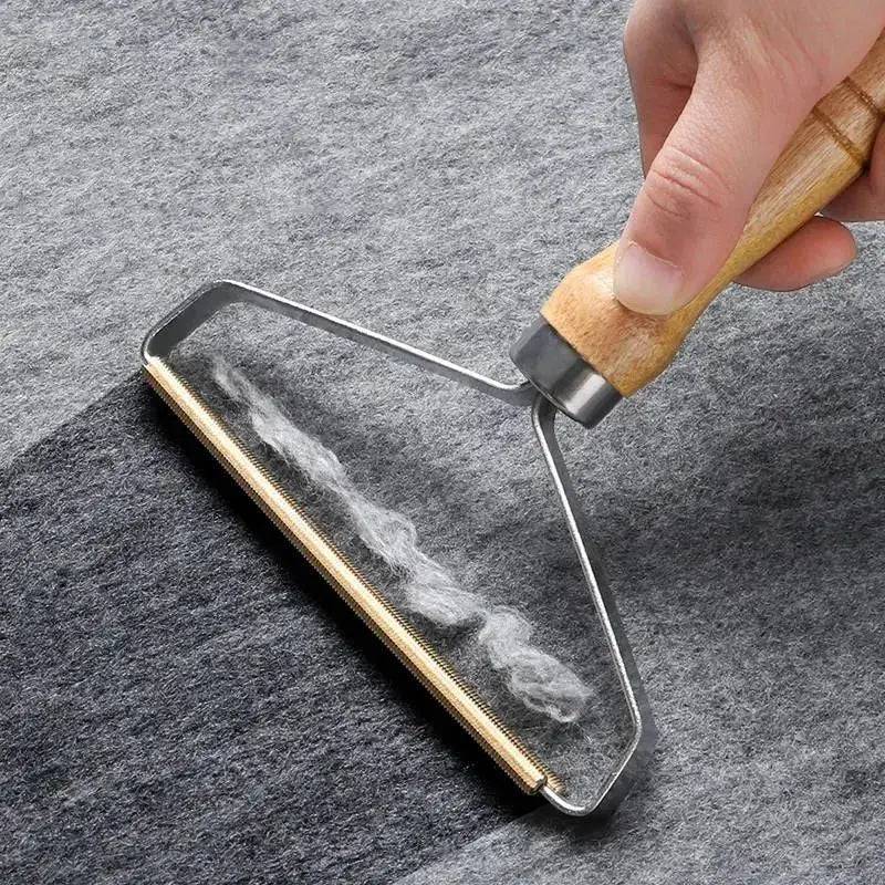 Wooden-handled pet hair remover and fabric shaver dragging a strip of white lint off gray felt.
