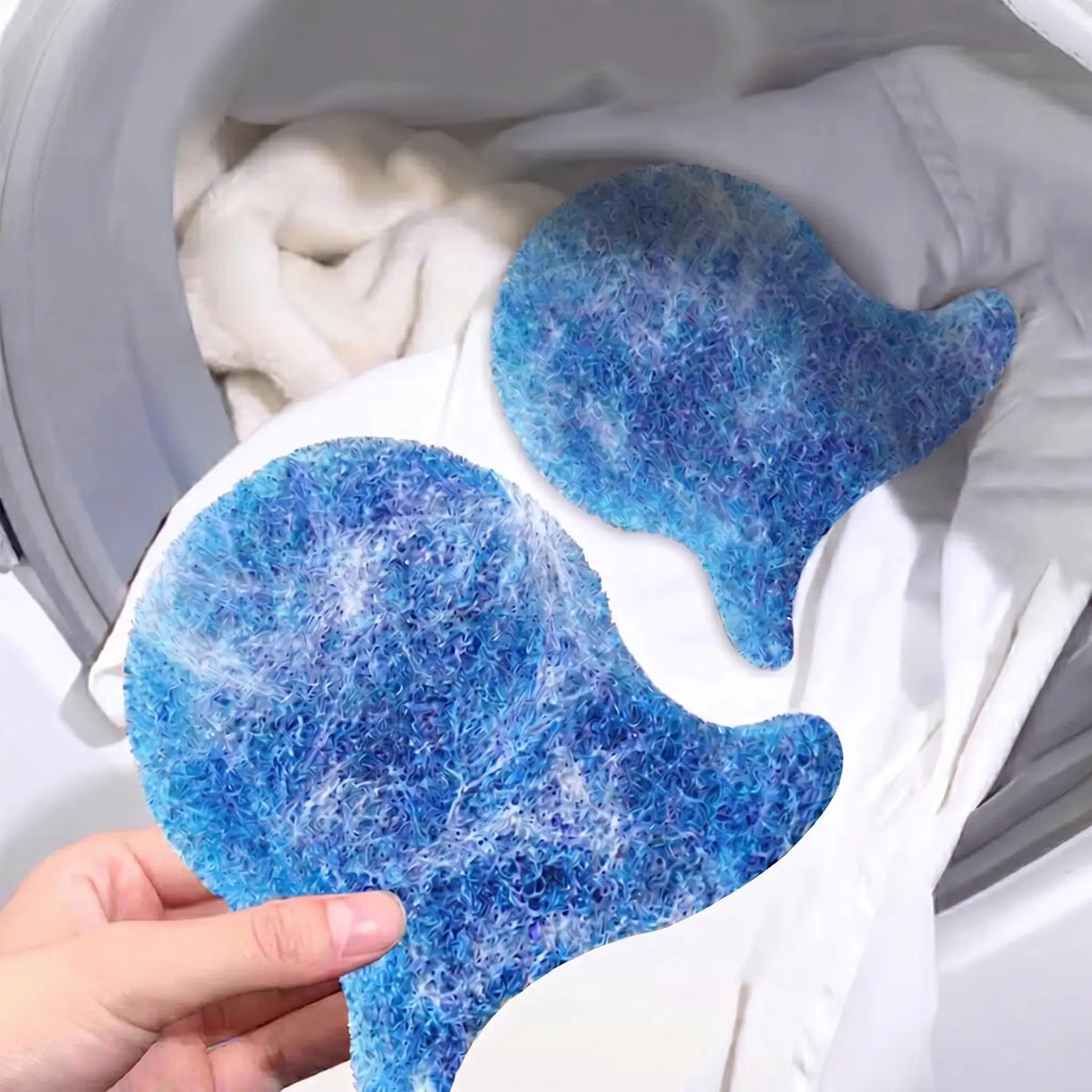 Two blue fish-shaped pet hair removers inside a washing machine drum with white laundry and the hair they collected.